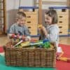 girl and boy children playing on green and red altas mat with a large wicker toy box in front of them